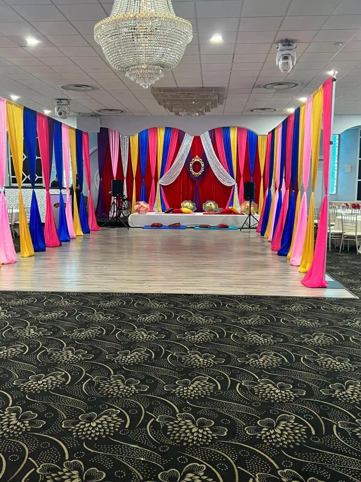 Sangeet stage hung with bright layered curtains and cushioned floor seating.