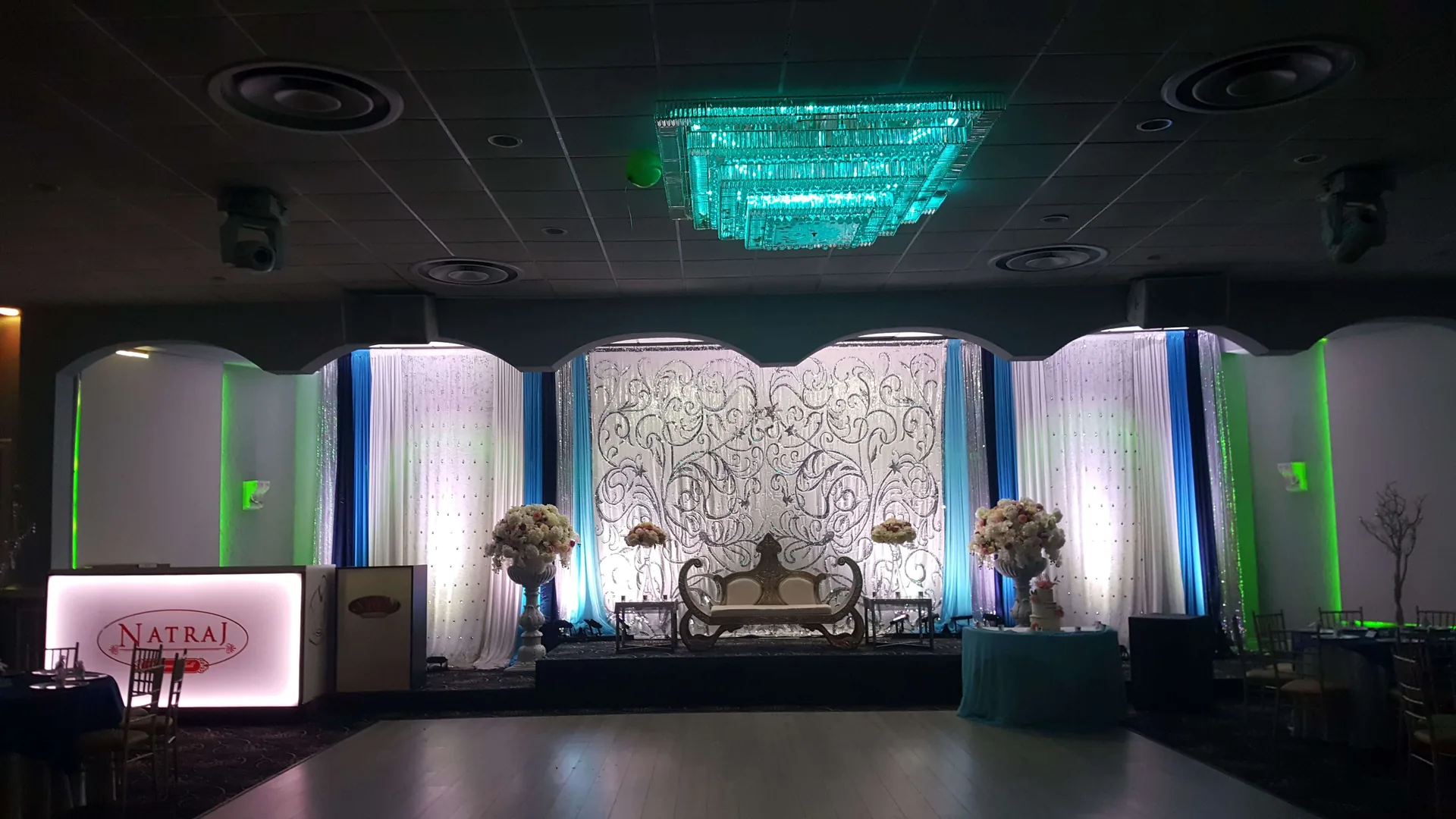 Stage lit in teal, with drapery falling behind the couple's seating.
