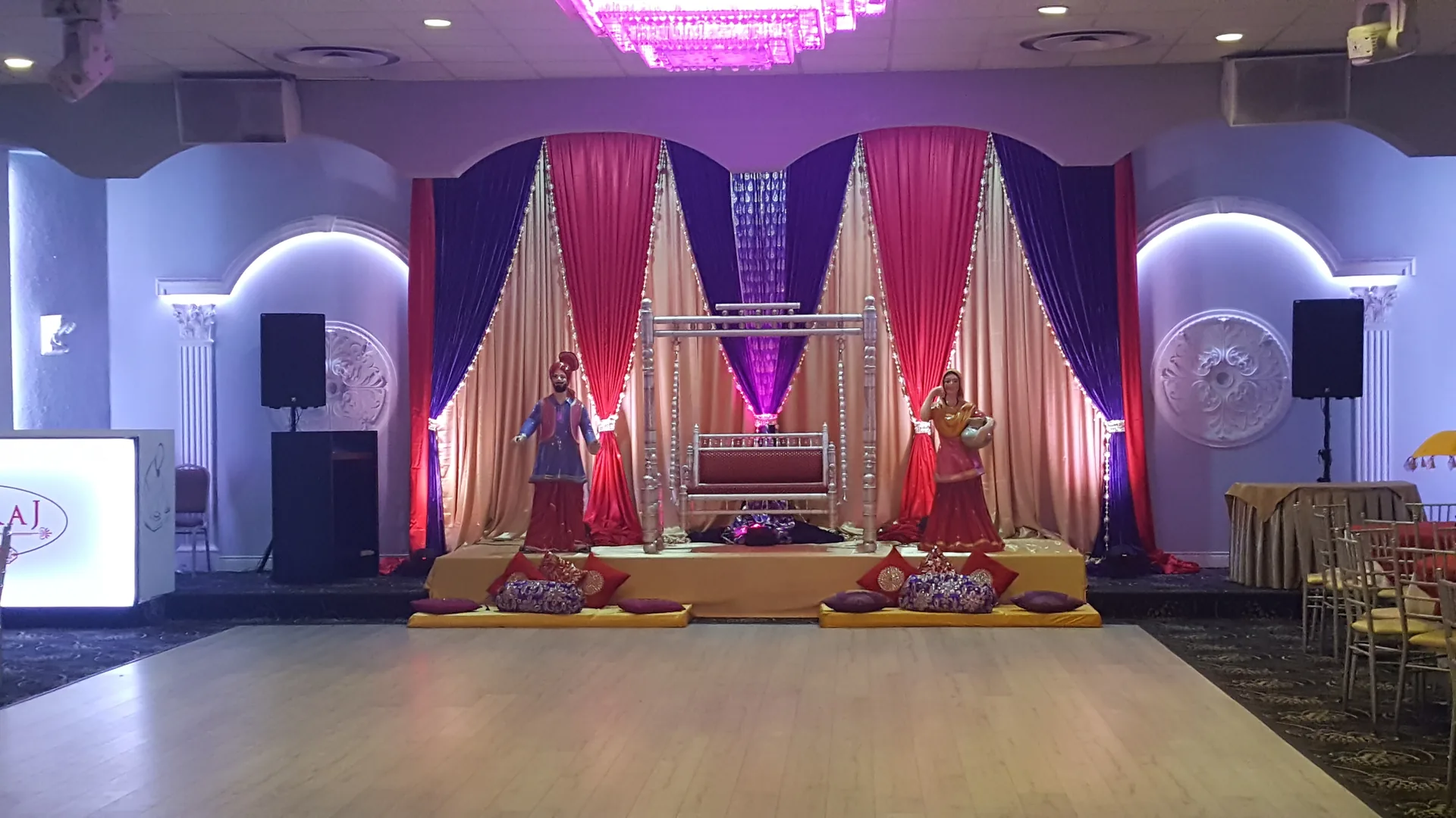 Decorated wedding stage with floral panels either side of the couple's seats.